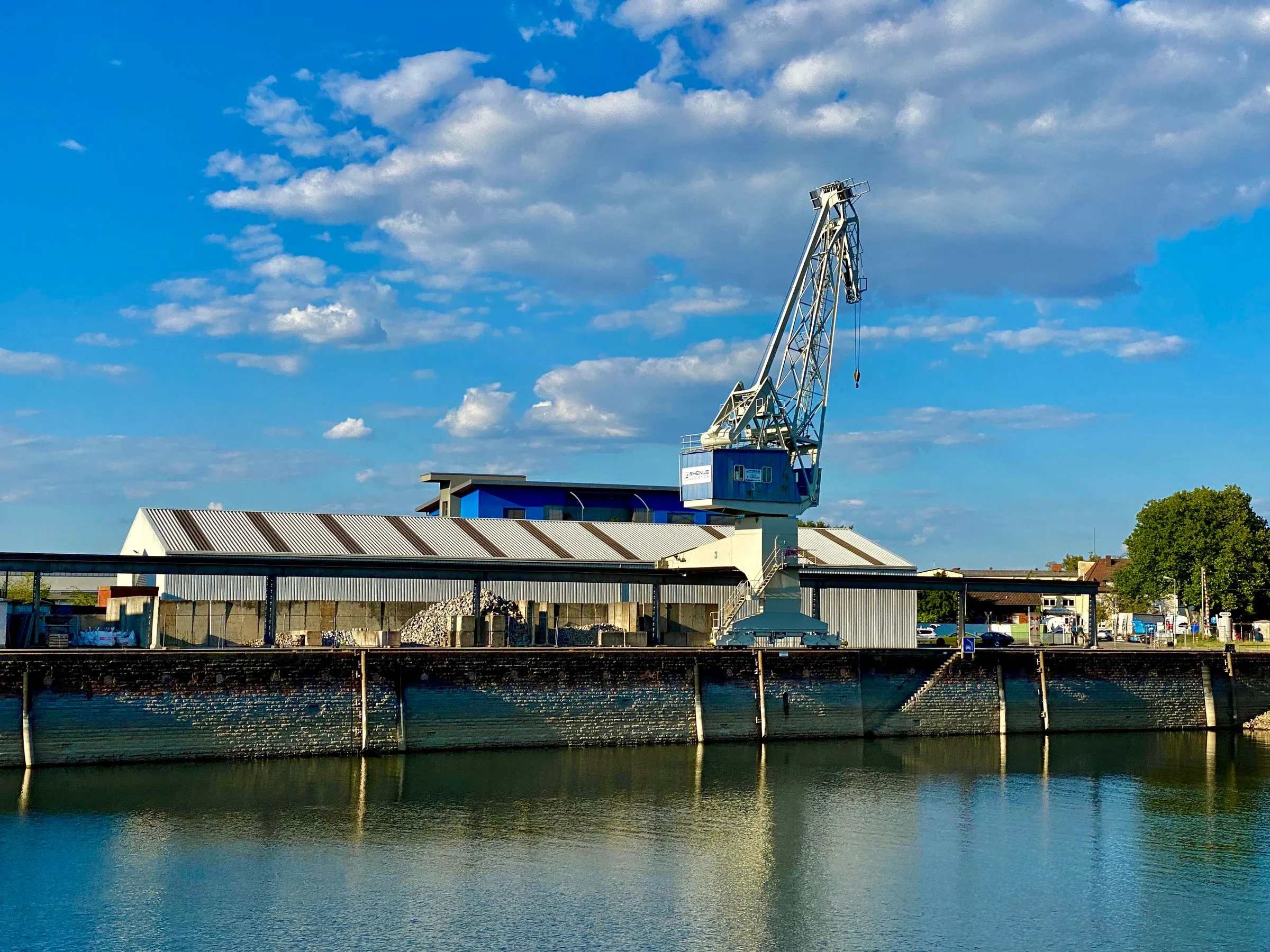 Hafenkräne und Lagerhalle am Rheinufer unter blauem Himmel